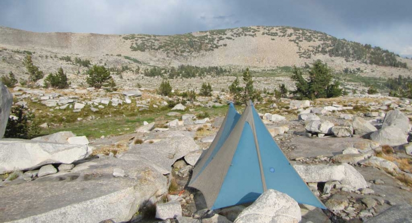 A tent rests on rocky terrain with a mountain in the background. 